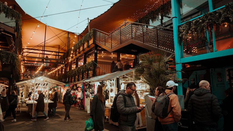 Browse more than a dozen market stall traders and check out daily events at Boxpark Camden. Credit: Eljay Briss. Image courtesy of Boxpark Camden. People walking past market stalls inside Boxpark Camden market.