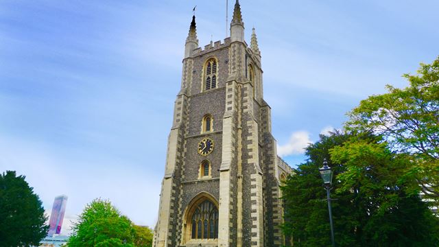 The main tower of Croydon Minster with trees on either side and blue sky in the background.