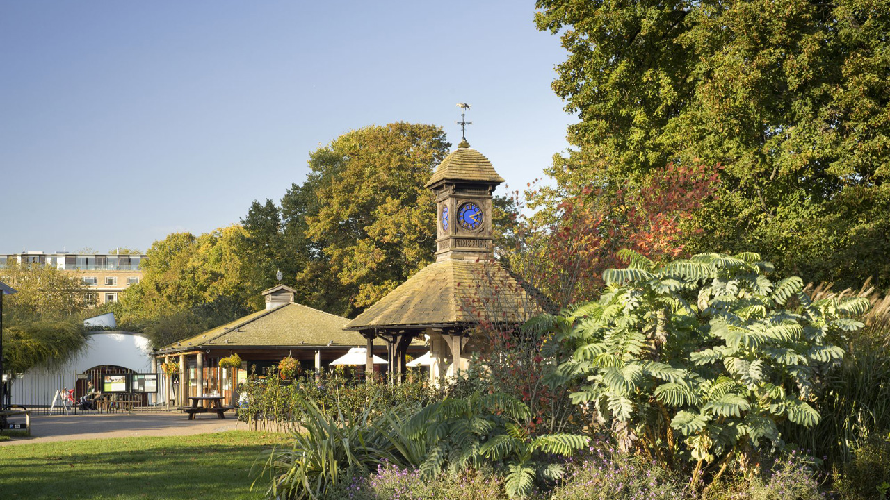 Diana Memorial Playground. Photo: Max Rush. Image courtesy of The Royal Parks. The entrance to the Diana, Princess of Wales Memorial Garden. There are leafy green trees in the foreground and a cafe further back.
