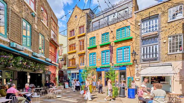 People sitting at tables or strolling though Neal's Yard on a sunny day.