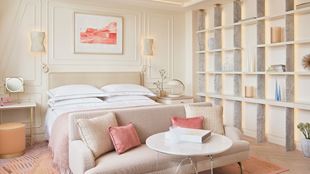 A deluxe room decorated in neutral colours showing a bed, sofa and shelves containing decorative objects.