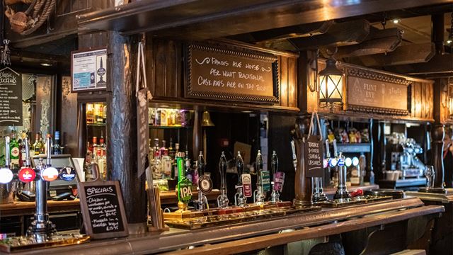 A close up of beer pumps on the top of the bar which has lots of bottles behind it.