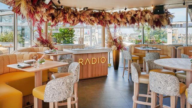 Chairs and tables in Radio Rooftop DJ area with full-length windows enclosing the space.