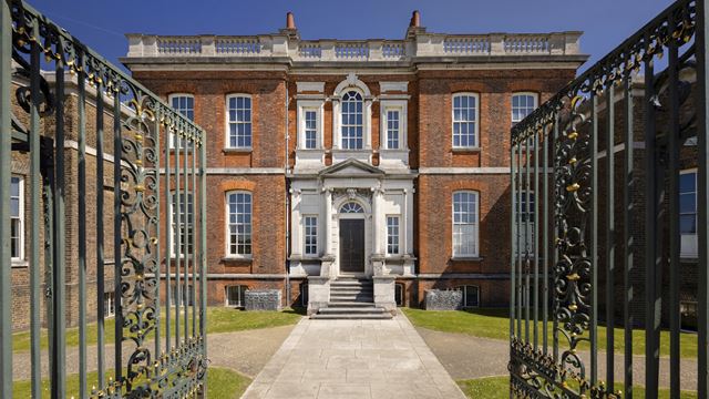 Gates open leading to brick-walled Ranger's House in Greenwich, with blue sky on a sunny day.