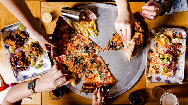 Hands take pizza slices and chips off of a silver tray.