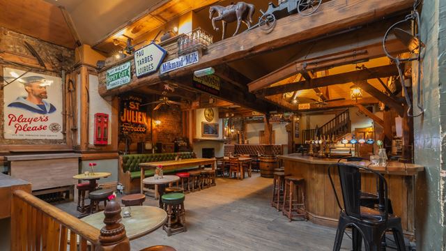 Inside the bar with a wooden bar in one corner and wooden tables and chairs taking up the rest of the space. There are old tin signs on the walls and beams.
