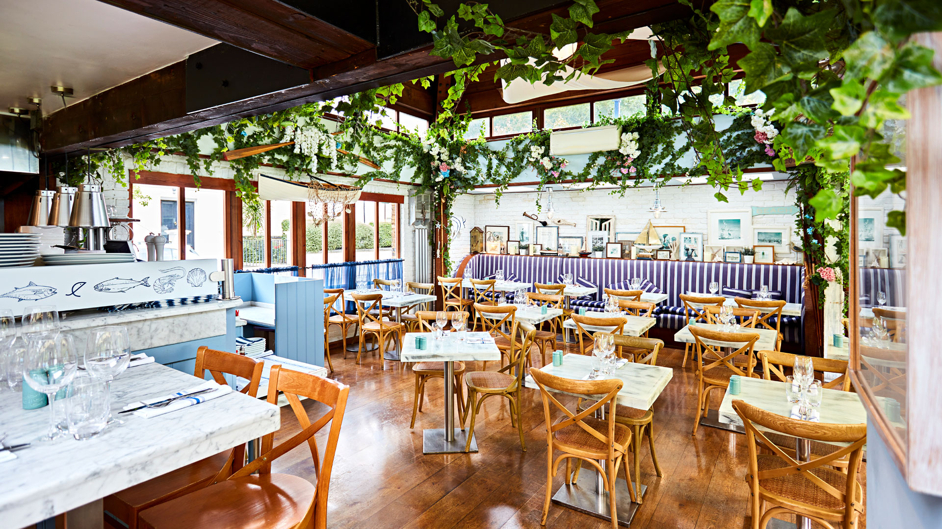 Marble-topped tables and wooden chairs inside The Summerhouse with plants trailing from the rafters.