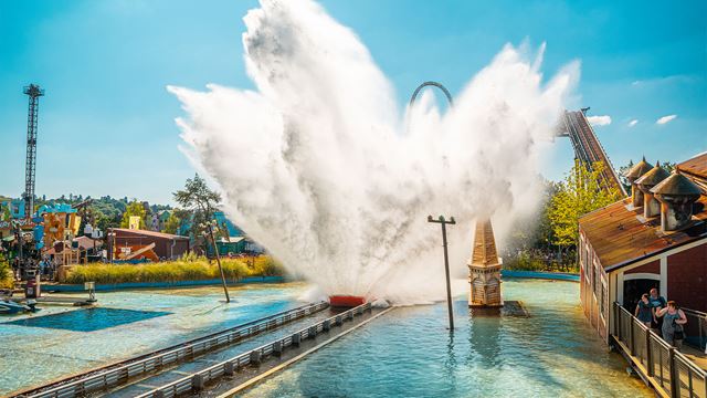 Landscape shot of two high rollercoasters and a water ride in the middle causing a big splash
