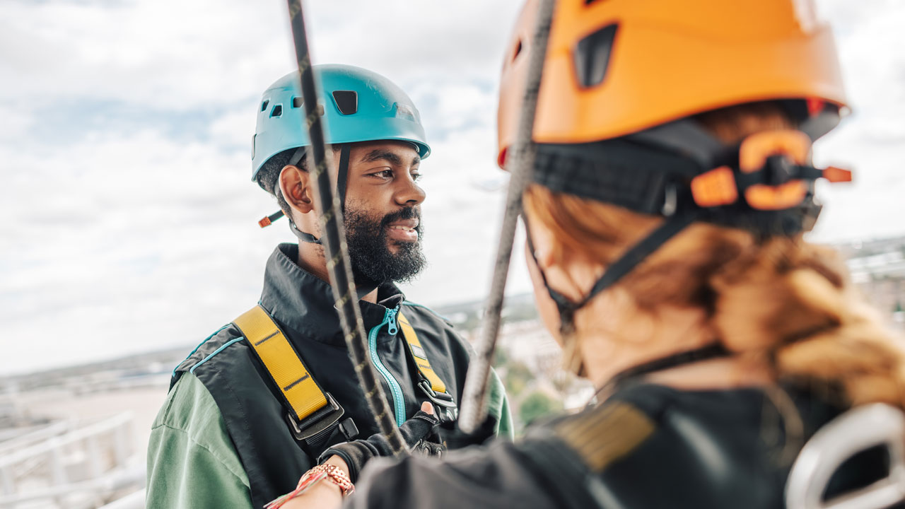 Grimpez au sommet du stade Tottenham Hotspur lors de l'expérience Dare Skywalk et retrouvez-vous à plus de 46 mètres de haut. © visitlondon.com/Michael Barrow Un homme portant un casque bleu et équippé d'un harnais se tiznt à côté d'une femme regardant le paysage depuis le stade de Tottenham Hottspur.