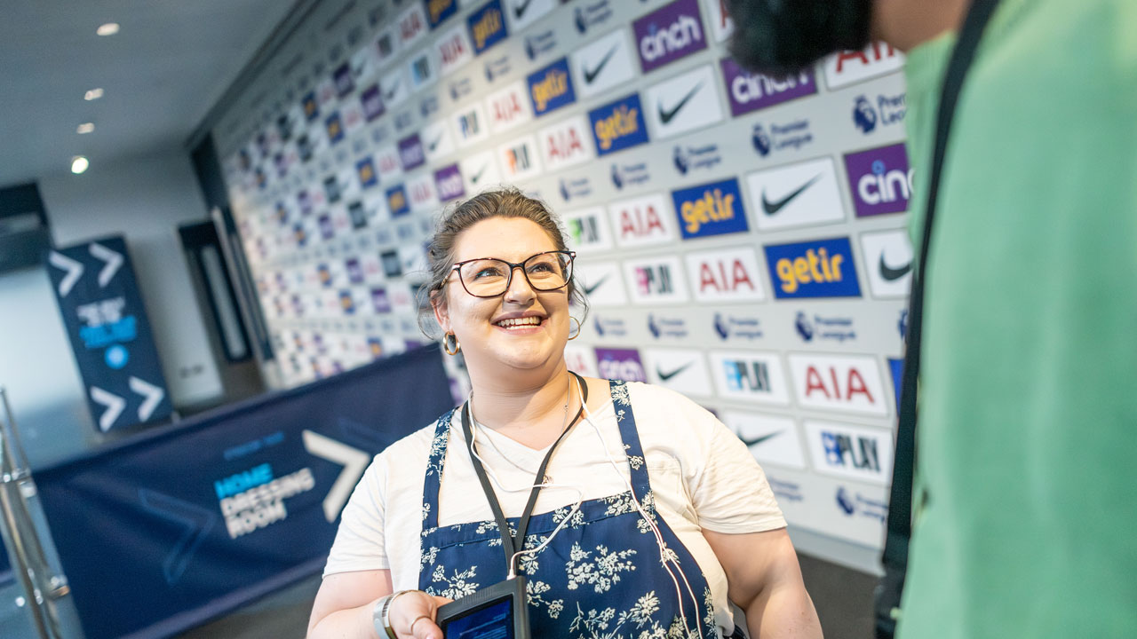 Récupérez votre guide audio en arrivant au stade de Tottenham Hotspur et profitez d'une visite à votre rythme. © visitlondon.com/Michael Barrow Une jeune femme sourit en regardant un ami lors d'une visite du stade de Tottenham Hotspur sur Londres.
