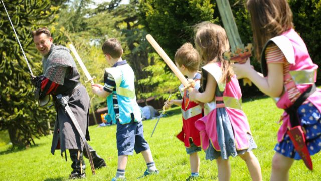 Ein Ritter zeigt Kindern auf der Burg Warwick, wie man ein Schwert verwendet. 