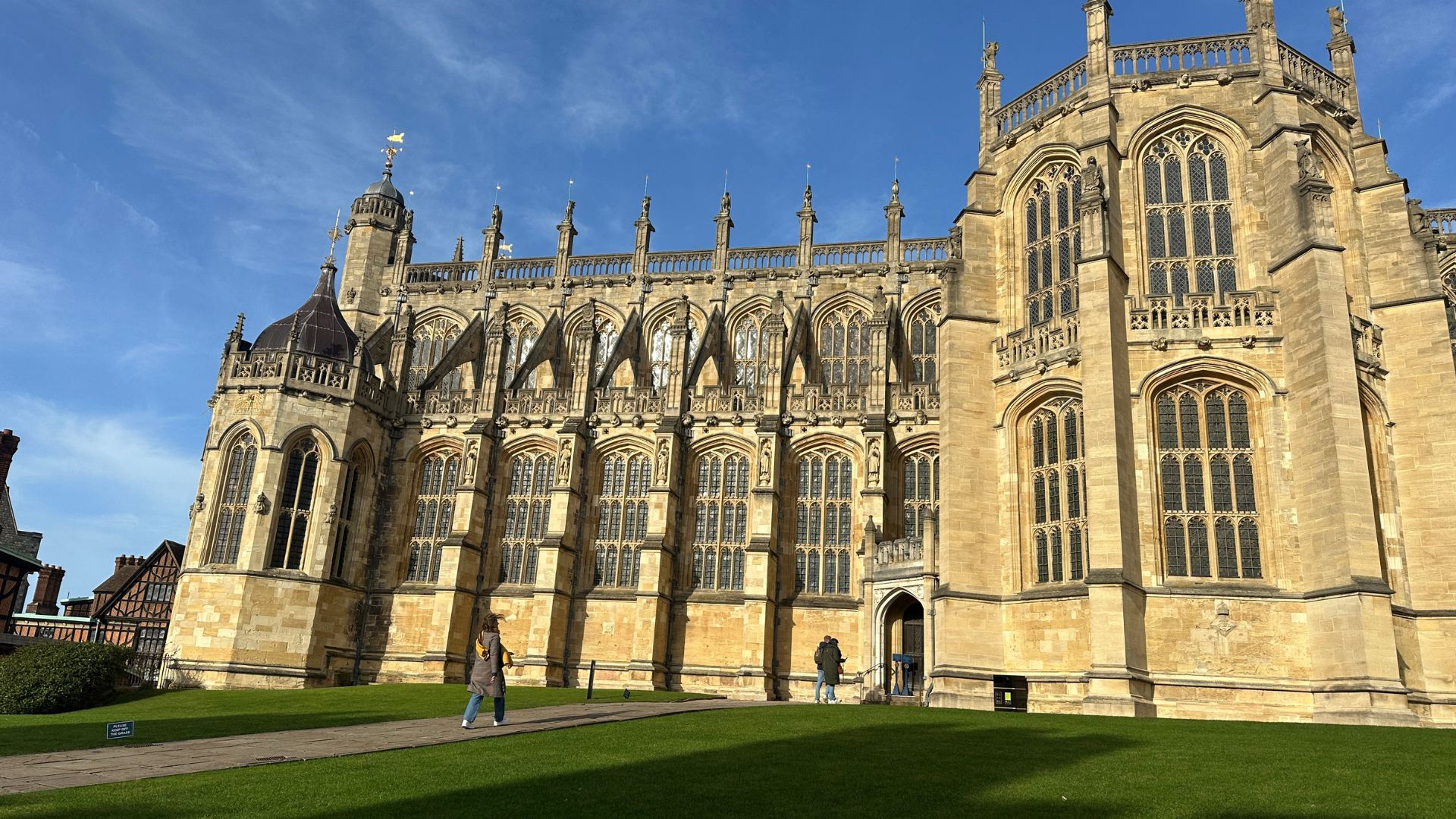A woman in a brown coat walks towards St George's Chapel at Windsor Castle on a sunny day.
