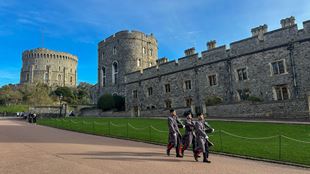 Three guards walk through the grounds of windsor castle.