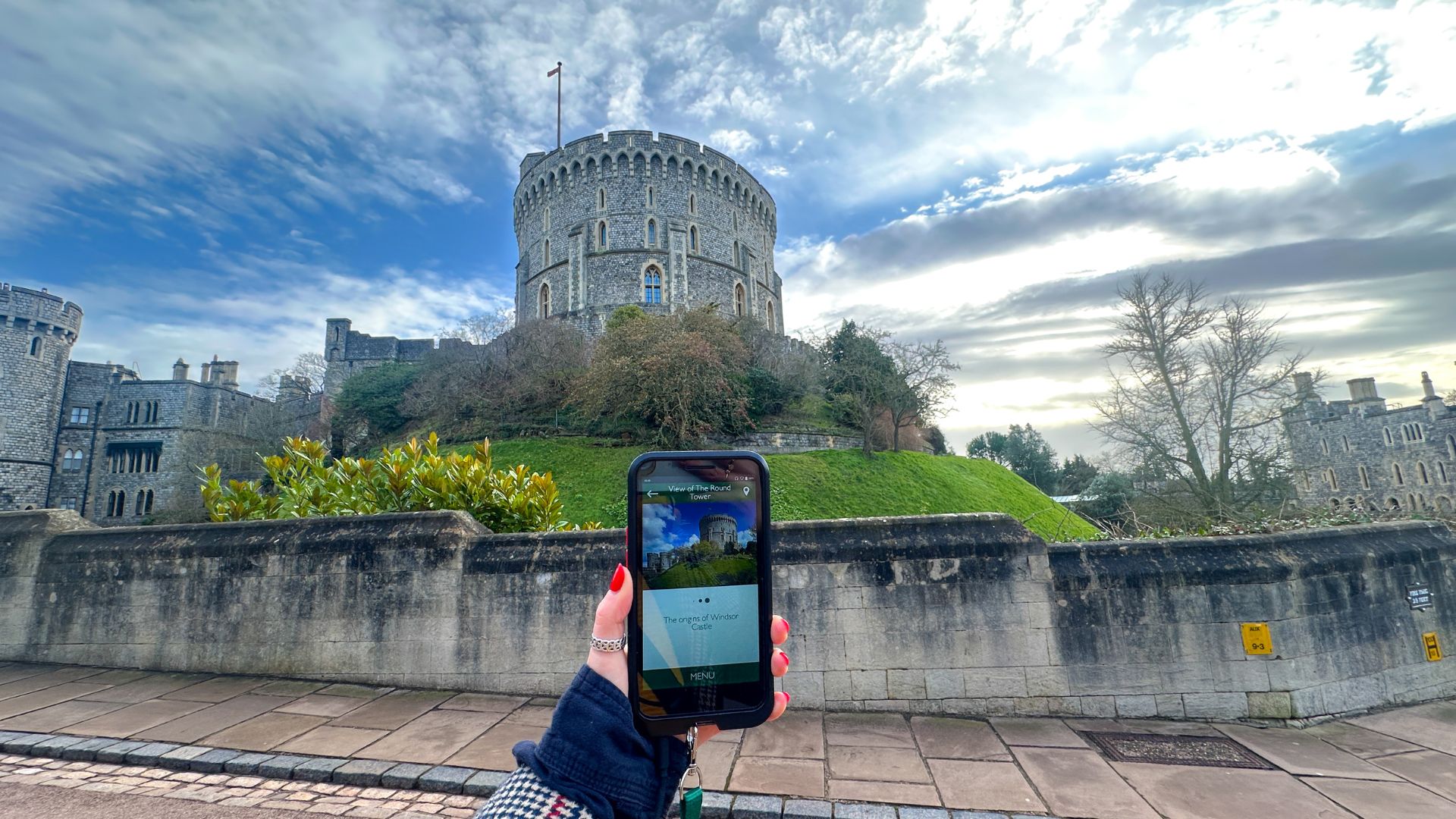 Use the audio guide to make your way around the castle. © Visit London/Kirstine Spicer A hand holds up the auido guide at windsor castle against the walls.