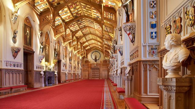 A long hall with red carpet and golden ceiling in st georges hall at windsor castle.
