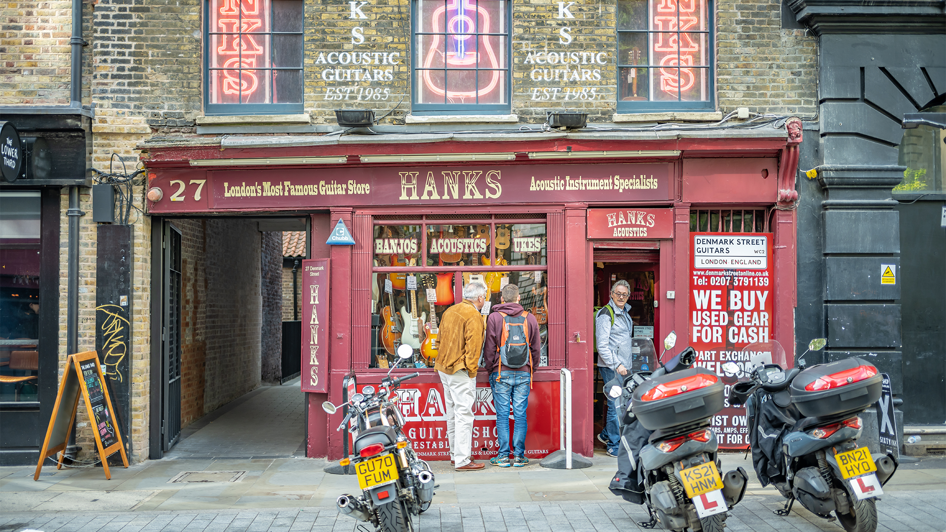 Red exterior storefront of Hank's Guitar Shop with three motorbikes parked up in front