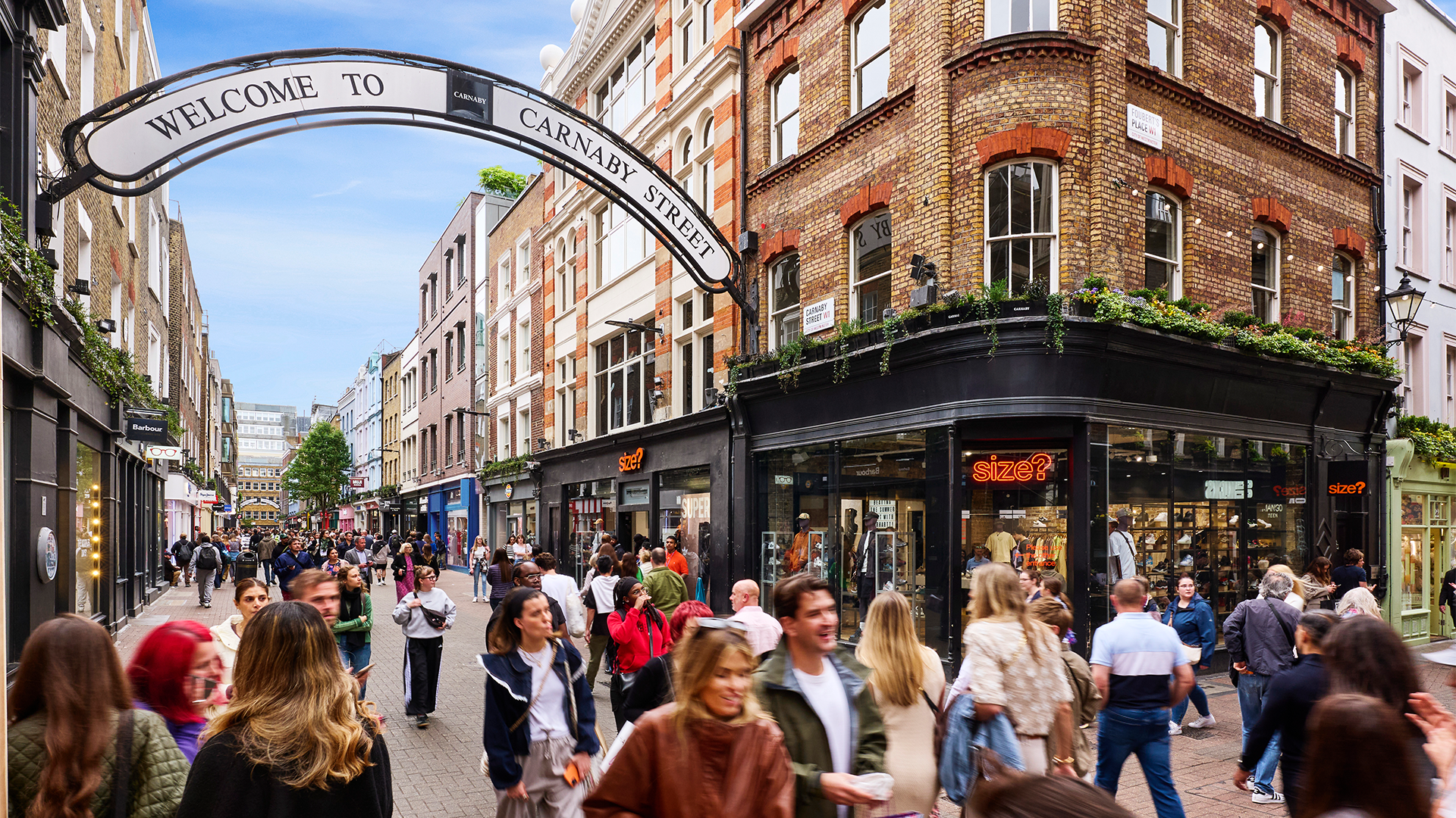 People walking through Carnaby Street with a welcome sign above