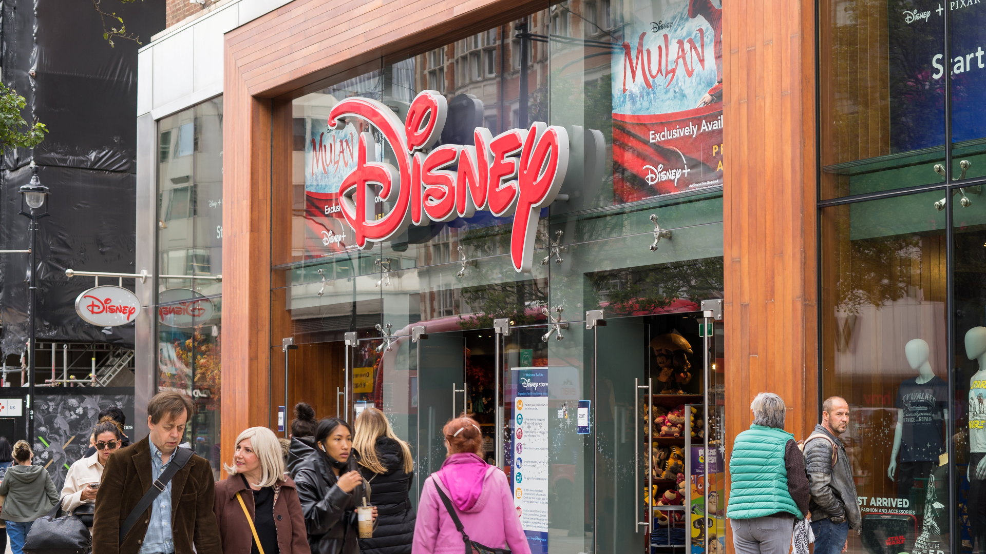 A view of the Disney Store on Oxford Street from outside with people walking in front of it and the giant red Disney sign above the doors