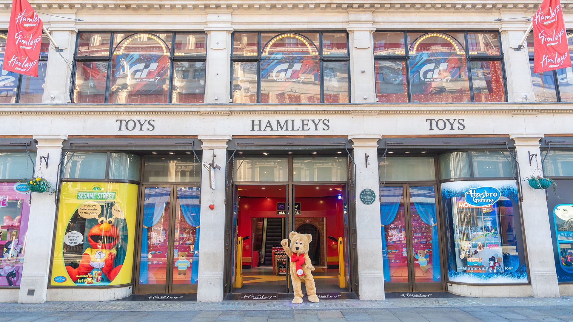 Discover 265 years of magic at Hamleys. Image courtesy of Hamleys. A giant golden bear with a red bow waving in front of Hamleys