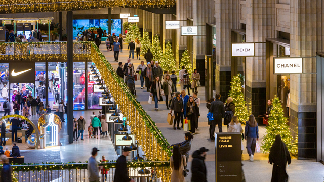 People walk around one of the many floors of shops inside Battersea Power Station adorned with Christmas decorations, with shop signs including Arcteryx, Reformation, SpaceNK and more lit up.