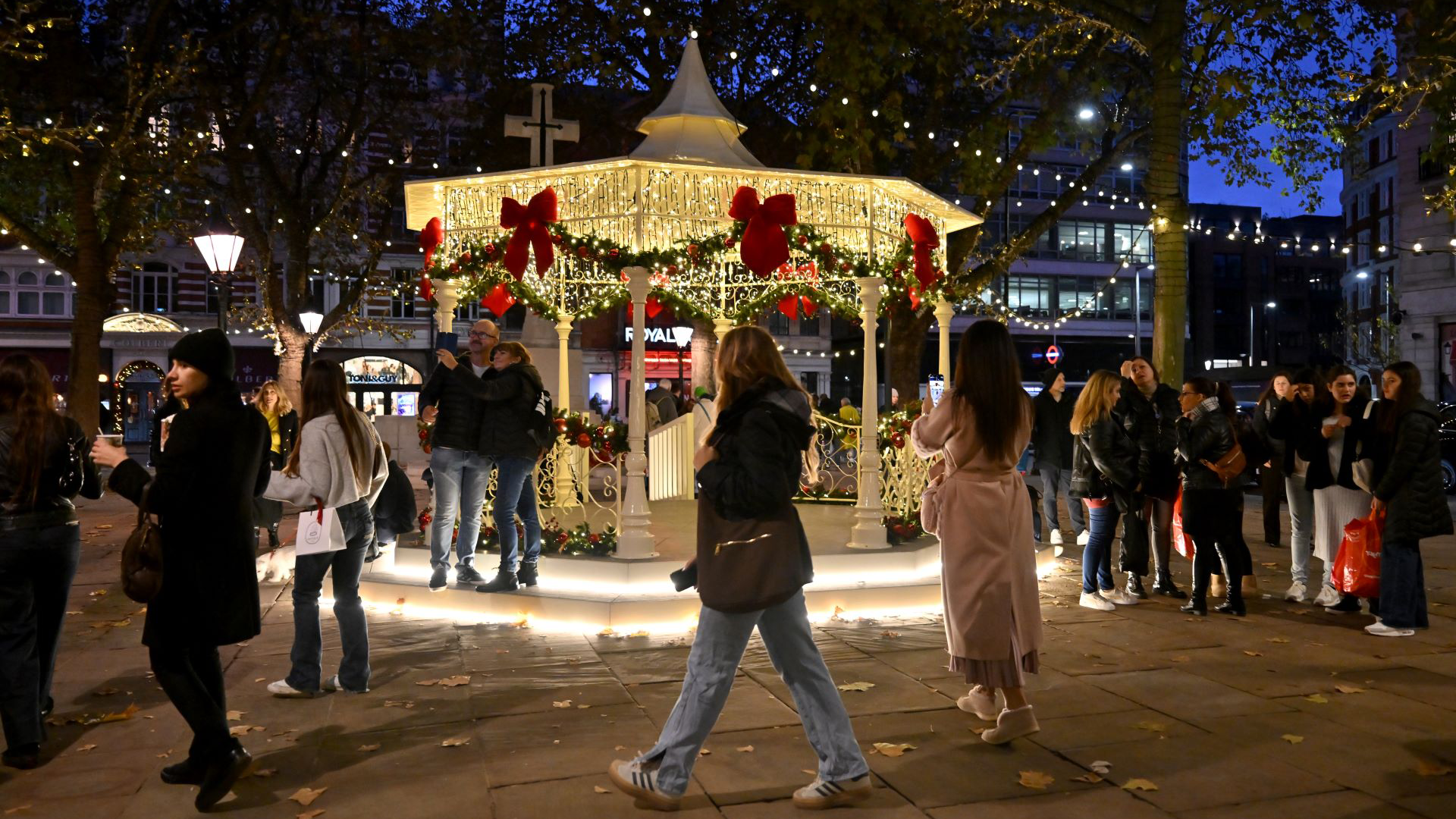 Head to Chelsea for a spot of luxury and high street shopping this Christmas. Credit: Chelsea. Image courtesy of Chelsea. A bandstand in the middle of a square in Chelsea lit up with warm twinkling lights and giant red velvet bows at night as people stroll past