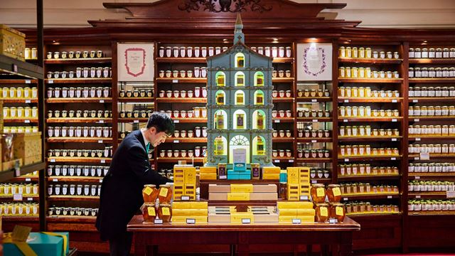 A shop assistant tidies the displays of Fortnum & Mason's food hall, with jars of pickles, chutneys and jams on shelving in the background.