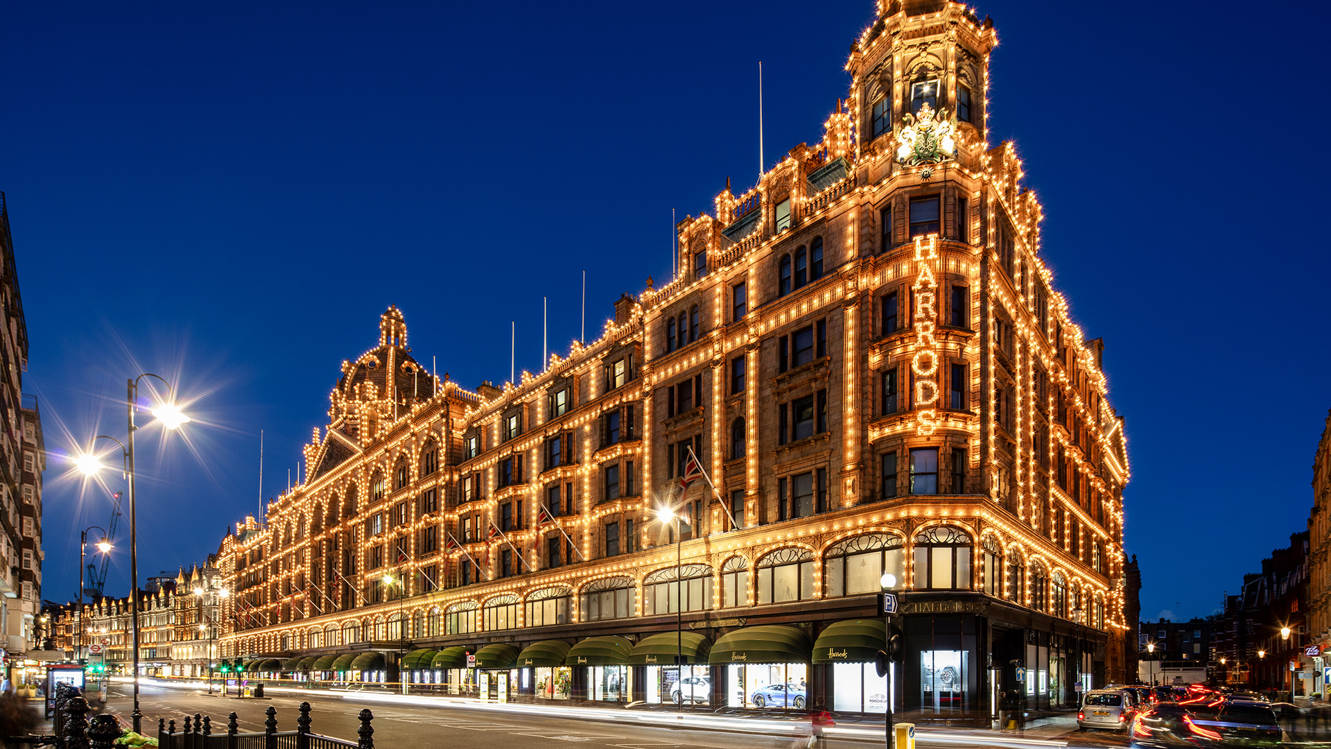 Harrods department store lit up at night against a dark blue sky and illuminated street lights in London.