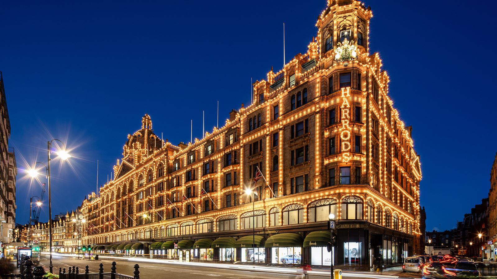 Harrods department store lit up at night against a dark blue sky and illuminated street lights in London.