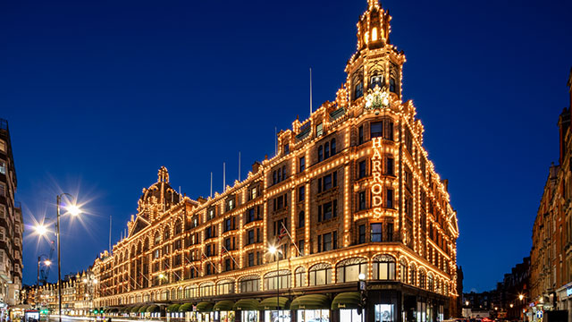Das Kaufhaus Harrods bei Nacht vor einem dunkelblauen Himmel und beleuchteten Straßenlaternen