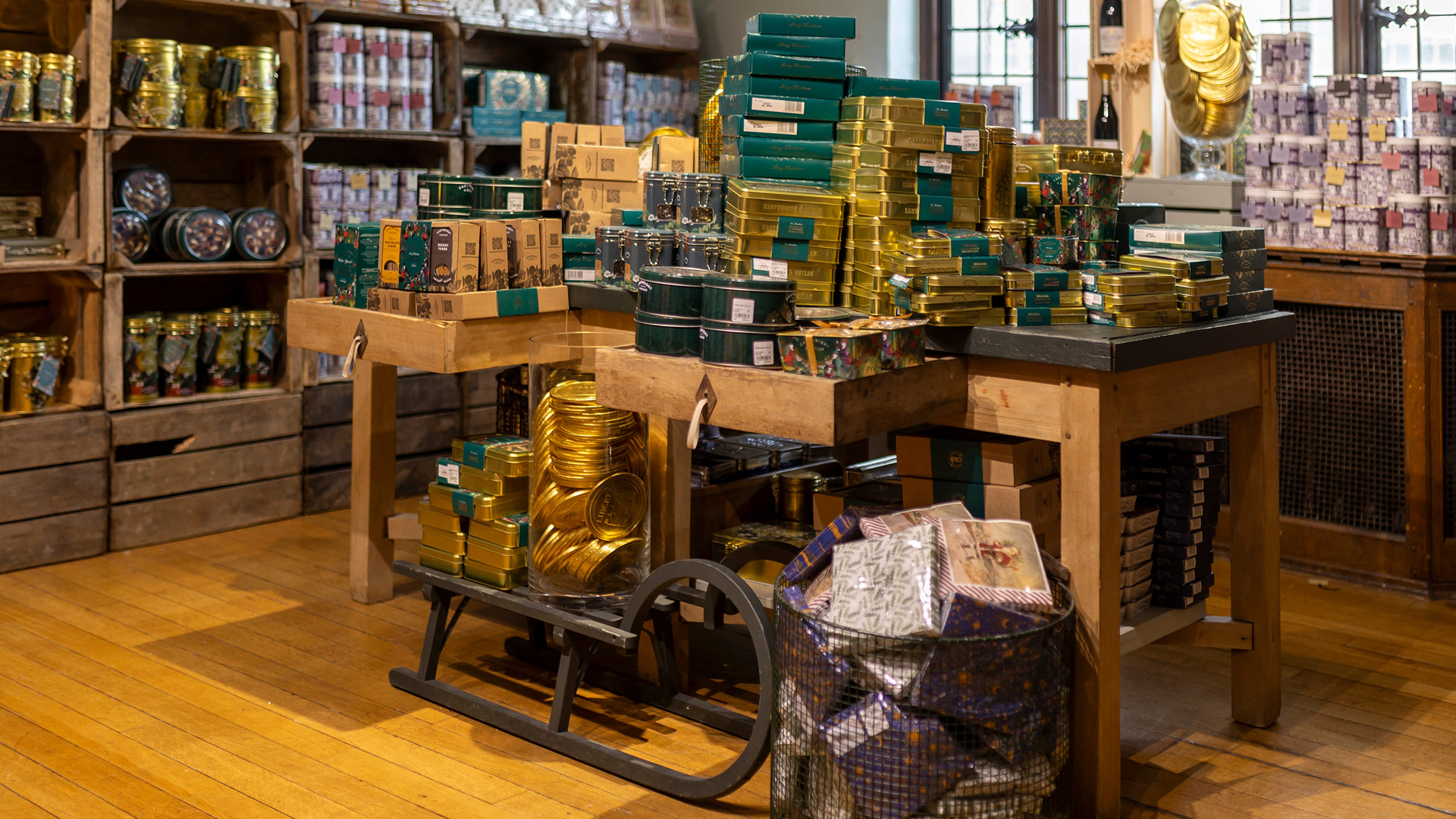 A selection of gold and green wrapped Christmas gifts in the corner of the store with a sledge carrying gold gifts in the foreground.
