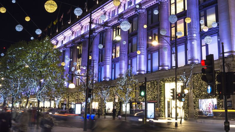 Kunden und Autos fahren an Selfridges vorbei, das anlässlich der Weihnachtszeit mit funkelnden Lichtern geschmückt ist. 