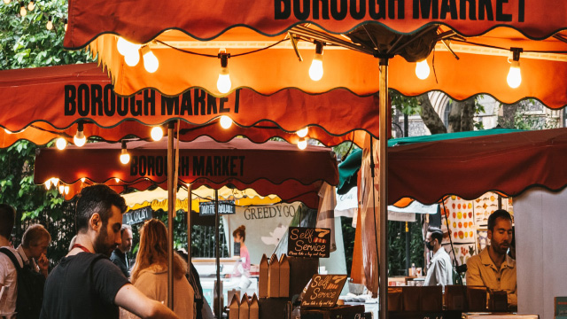 People shopping below orange umbrellas and bright lights in Borough Market, London
