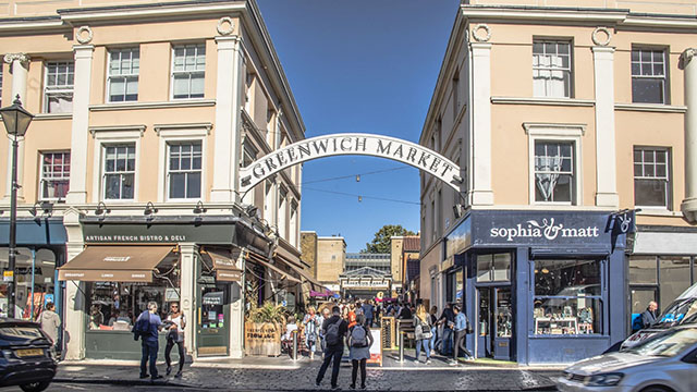 A couple stand in the street looking at the entrance to Greenwich Market.