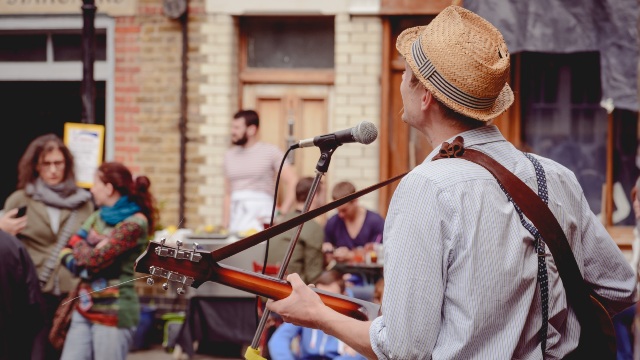 Street musician singing and playing the guitar to a small crowd on Columbia Road.