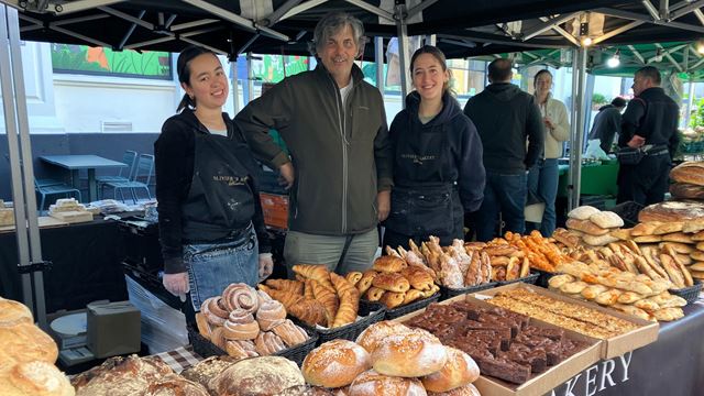 Team at Olivier’s Bakery at Venn Street Market standing behind a selection of bread, croissants, cakes and pastries.