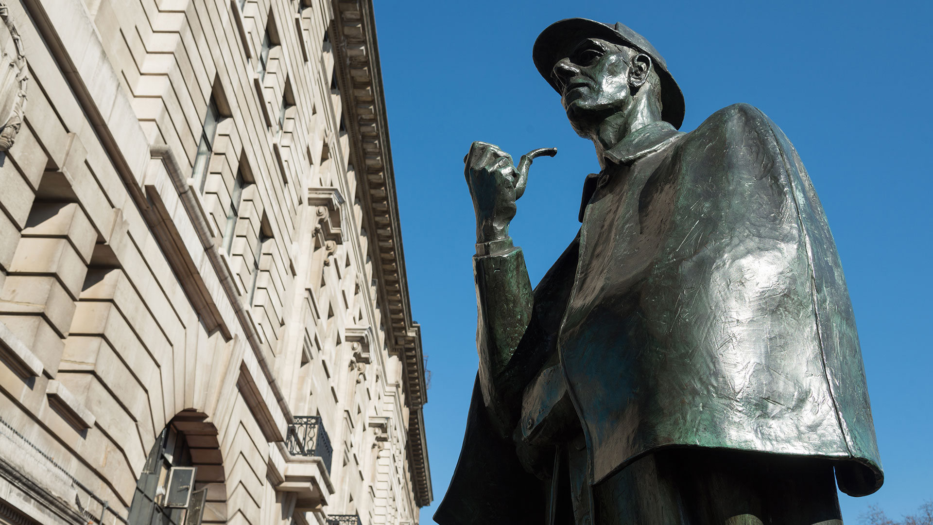 Statue of Sherlock Holmes smoking a pipe outside Baker Street station on a sunny day.