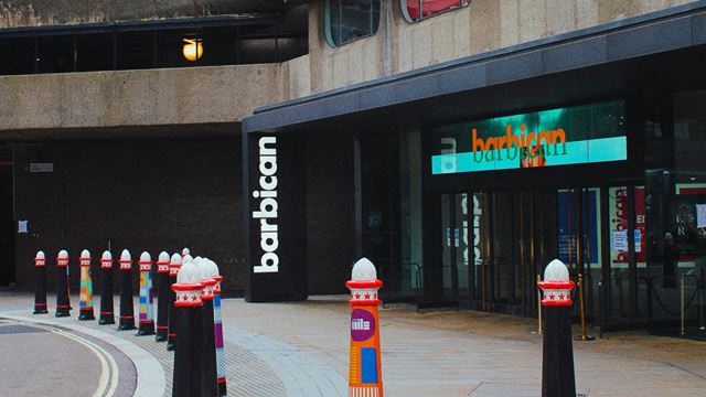 Exterior of the Barbican Centre, with black glass doors and colourful bollards in front.
