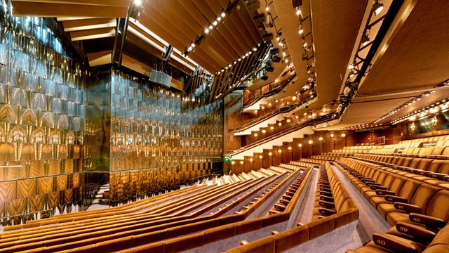 Modern, brutalist auditorium with brown velvet seats and a stage with a mirrored backdrop.
