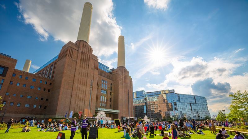 Explore Battersea Power Station in the summertime. Image credit: London & Partners/Peter Cohen. Image courtesy of London & Partners. Visitors sitting on the grass outside Battersea Power Station on a sunny day.