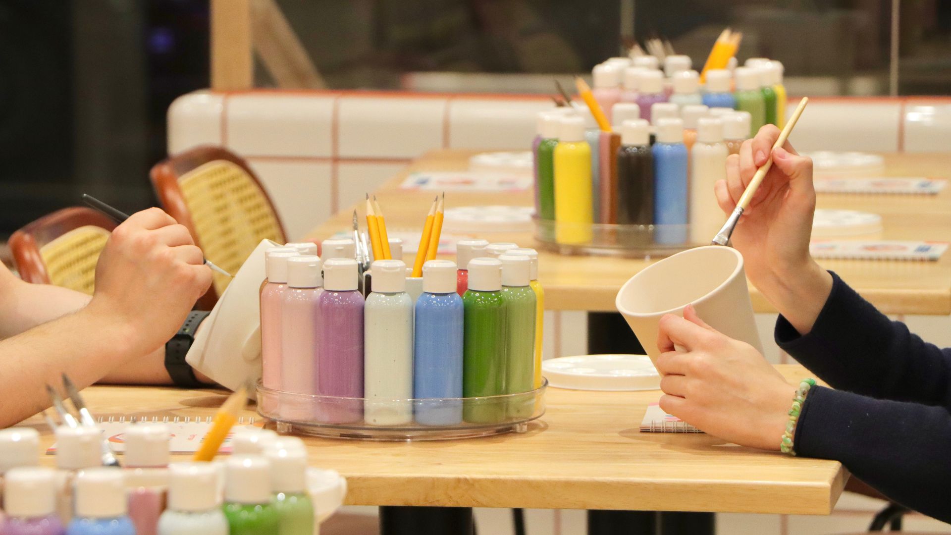 Slow things down and get creative with a relaxed pottery painting session. Image courtesy of BonBon Pottery. People painting ceramics at a table with colourful paints and brushes laid out.
