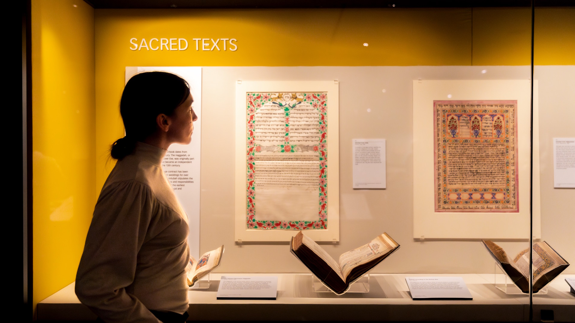 A person looks at sacred texts, displayed in a glass cabinet, held within the Treasures Gallery at the British Library.