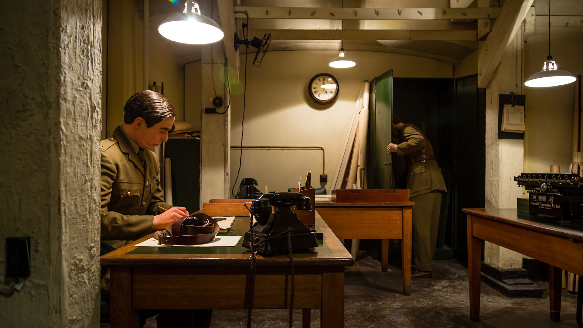 Underground bunker in the Churchill War Rooms, where a mannequin in a khaki army uniform sits at a table writing a report.