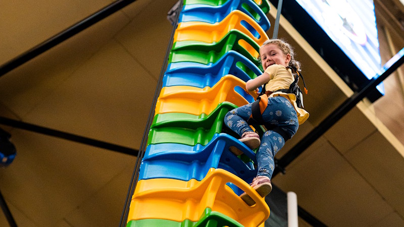 A young girl looking down as she climbs a multicoloured climbing frame at Clip 'n Climb.