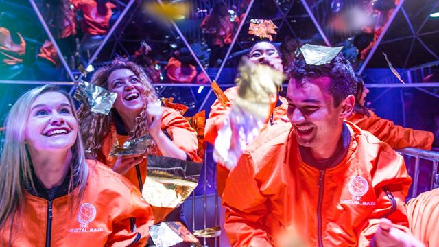 Group of people in orange jackets smiling inside the Crystal Dome of The Crystal Maze LIVE Experience in London.