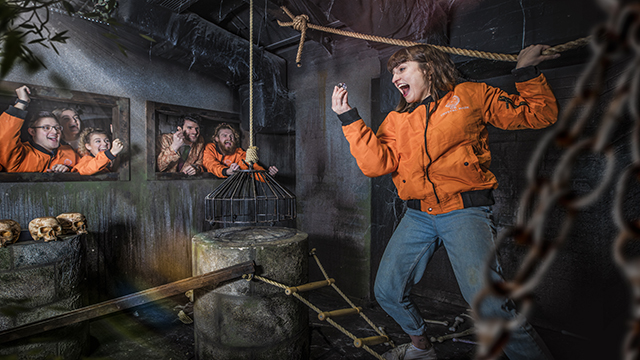 A woman wearing an orange jacketis cheered up by her team after finding a clue in a dungeon