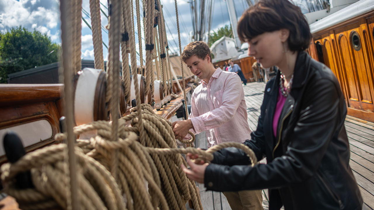 Explorez le pont supérieur du navire The Cutty Sark, et prenez le temps d'admirer son design spectaculaire. © visitlondon.com/Michael Barrow Un homme et une femme se trouve sur le pont supérieur du Cutty Sark et s'essayent à faire des noeuds de corde marins.