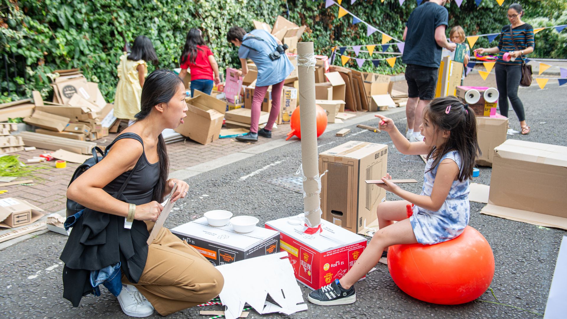 A mum and child play outdoors creating a monster out of cardboard and other materials at the Discover Children's Story Centre.