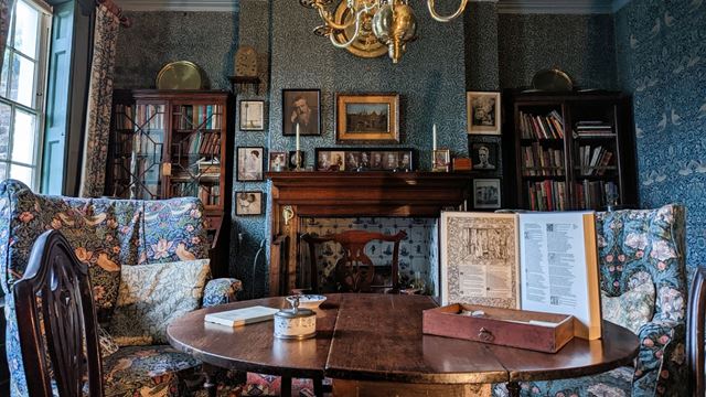 Interior of Emery Walker’s House, showing a richly decorated dining room with bookshelves, patterned furnishings, a fireplace and brass chandelier.