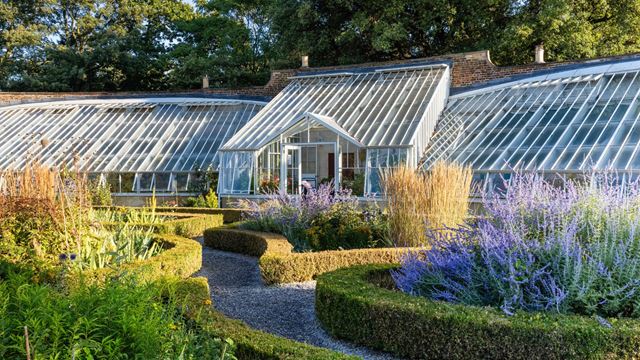 Historic glasshouses surrounded by colourful flower beds and neatly clipped hedges at Fulham Palace.