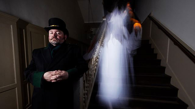 Un garde se tient devant un escalier avec une apparition fantomatique se tenant derrière lui.